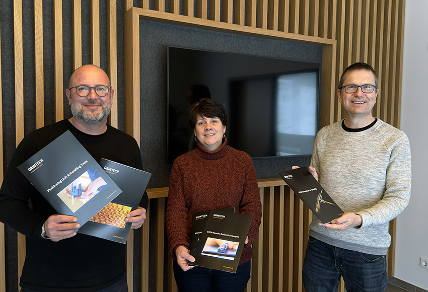 Drei Mitarbeitende der Firma Grintech halten einen Messekatalog hoch.