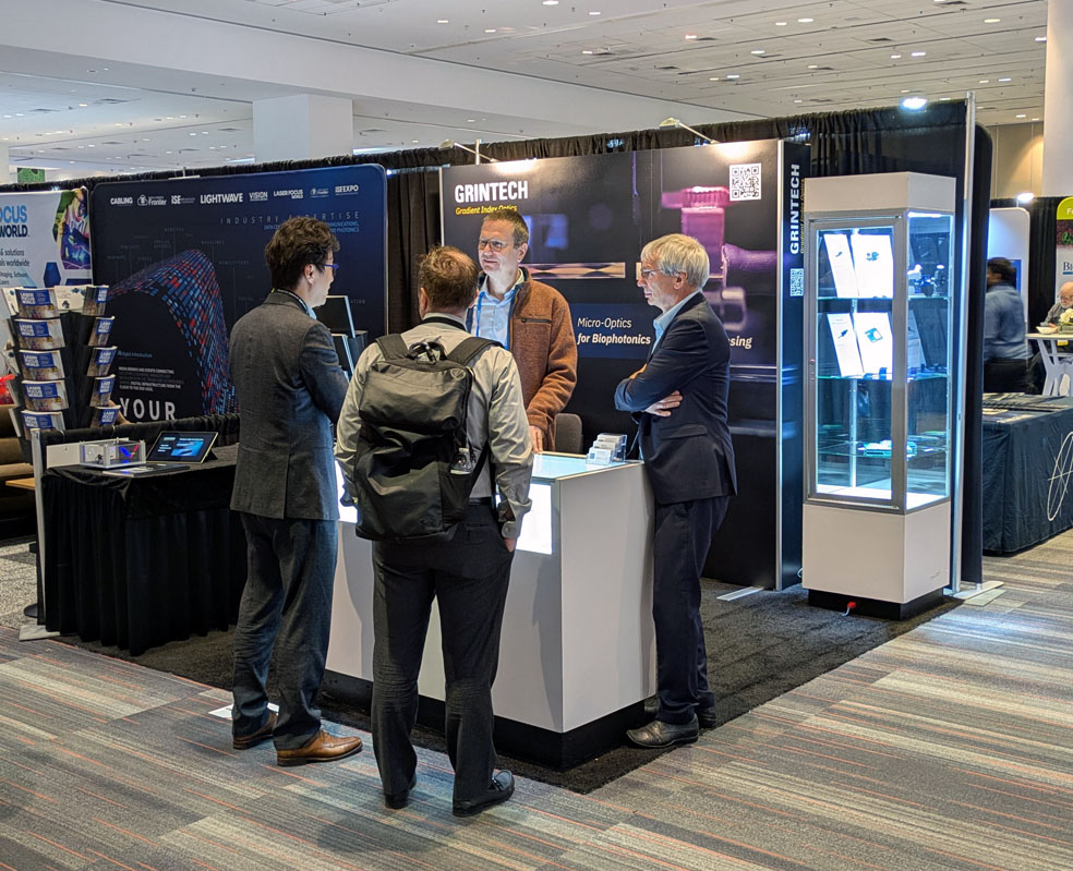 Zwei Männer hinter einem Messe-Tresen unterhalten sich mit zwei Messebesuchern auf der Photonics West 2026