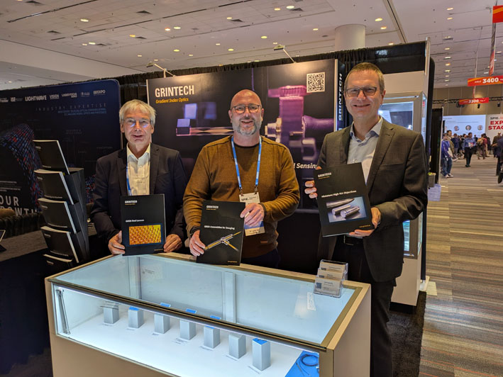 Drei Herren stehen an einem Messestand hinter einem Tresen.